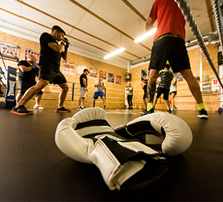 White boxing gloves on mat next to boxers training